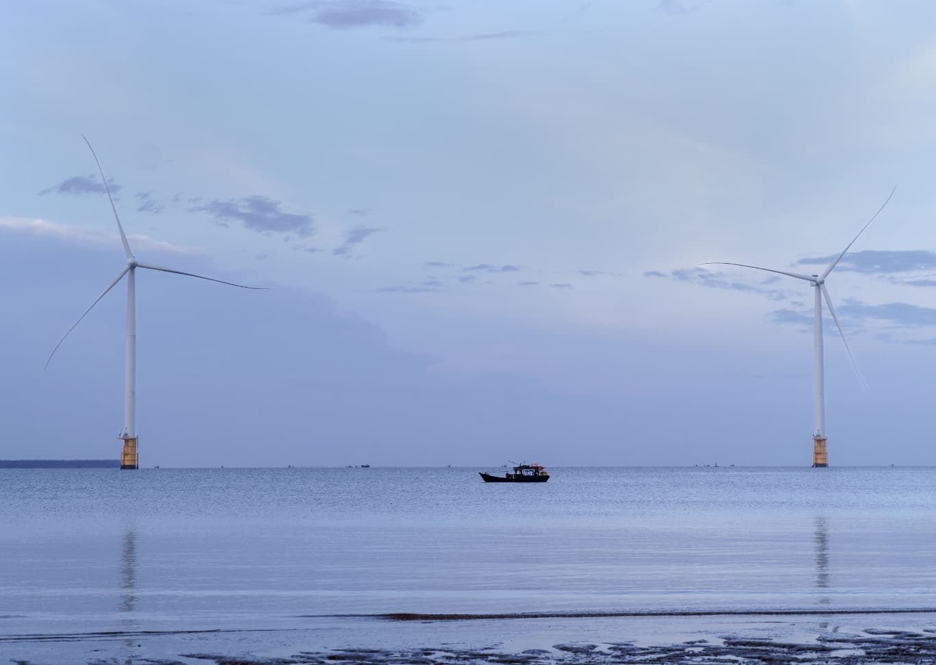 Two wind turbines and a traditional boat near a shore